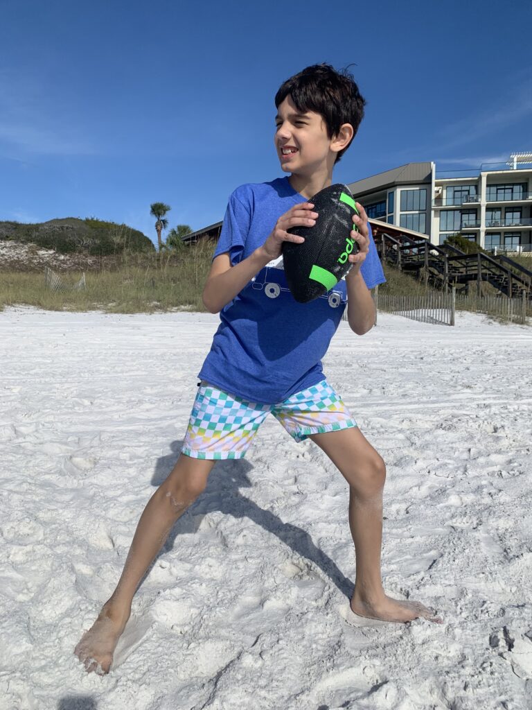 Young boy playing football on the beach